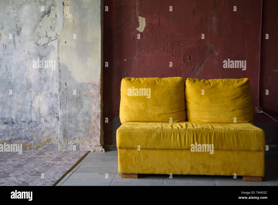 Желтый диван на фоне кирпичной стены