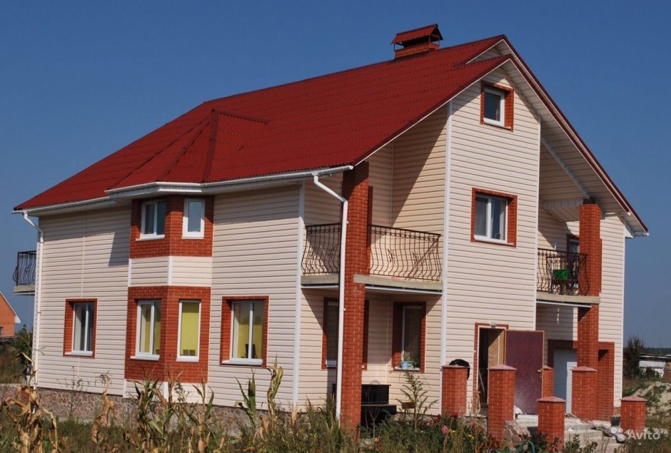 Отделка камнем фасада дома с красной крышей